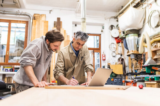 Male colleague with laptop writing while working at workshop