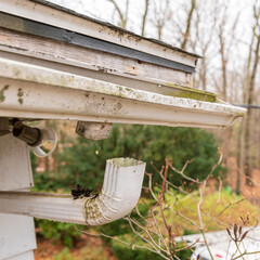 Close up of water dripping from the detached gutter that is clogged and pulled of the side of the...