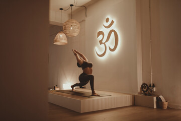 Female yoga instructor with arms raised bending while practicing by Om symbol