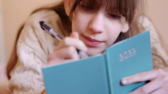 Teenage Girl Lying On Bed At Home Writing Resolutions In New Year 2022 Diary 