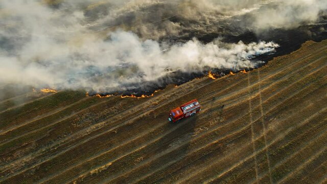 Cinematic shot fire truck and firefighters on burning field with dry stubble and smoking flame. Emergency case for danger mission and rescue nature saving concept