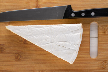 One delicious slice of brie cheese with a knife on a bamboo board, close-up, top view.