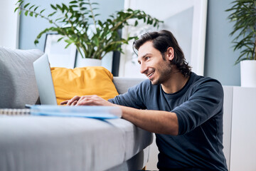 Smiling male student using laptop while learning at home