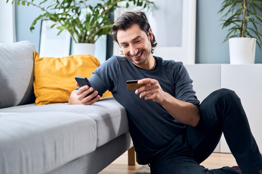 Smiling Man With Smart Phone Shopping Online Through Credit Card At Home