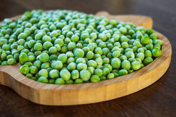 frozen frosty green peas on wooden plate closeup