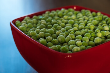 frozen frosty green peas in red ceramic bowl closeup