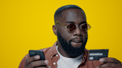 Closeup bearded afro guy using credit card for online payment in studio.