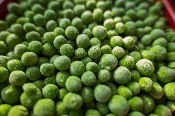 frozen frosty green peas in red ceramic bowl closeup