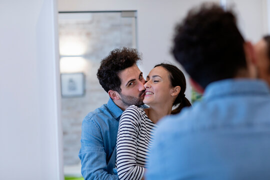 Boyfriend kissing girlfriend on cheek in front of mirror at home