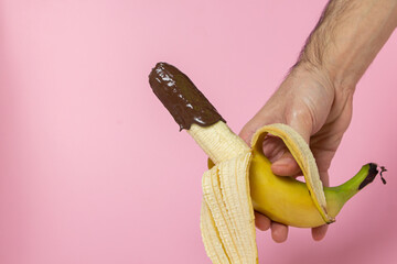 Banana in chocolate on a pink background. Hand holds a banana poured with melted chocolate. Fruit...