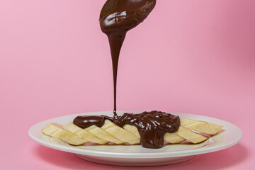 Banana in chocolate on a pink background. Pour melted chocolate onto banana slices. Fruit dessert