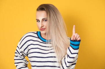 Young woman pointing up with forefinger to copy space - blank space for text, isolated on yellow background