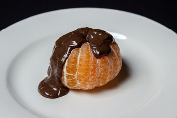 Tangerine in chocolate on a black background. Peeled tangerine topped with melted chocolate. Fruit dessert