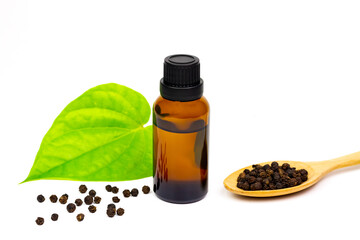 Black pepper essential oil in glass bottle with peppercorn on wooden spoon and green leaf isolated on white background.
