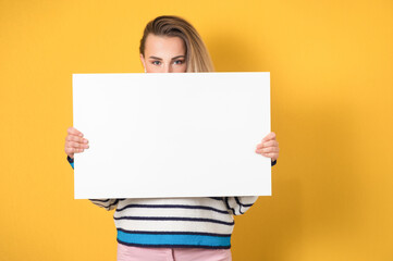 Young women holding white board, isolated on yellow background. Promoting girl showing blank empty paper billboard with blank space for text