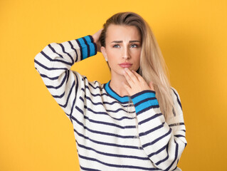 Pensive young woman being in confusion with arms on head, isolated on yellow background