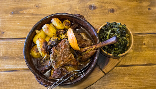 Roasted goatling or roasted kid "cabrito assado" ready to eat on a wooden table. Served with roasted potatoes and sprouts. Typical portuguese dish