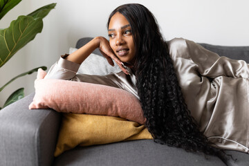 Woman with long black hair lying on sofa while day dreaming at home