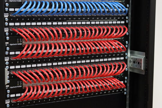 Ethernet switches are connected to patch panels using colored patch cords in the data rack.