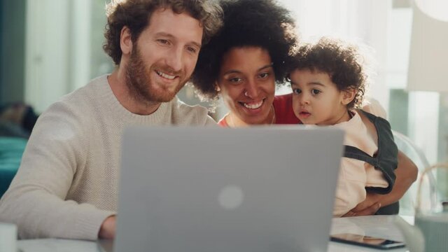 Father, Mother and Young Son Use Laptop Computer at Home Apartment. Happy Mixed Race Family with Loving Child Watch Cartoons, Shop Baby Products Online, Look at Funny Pictures or Play Video Games.