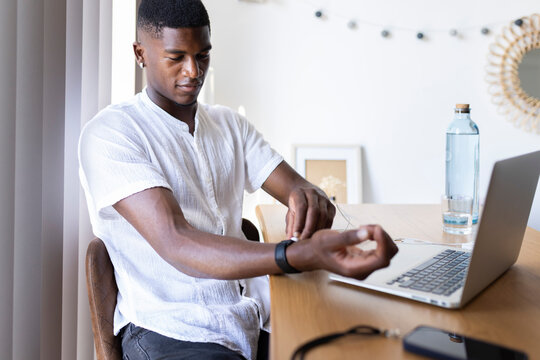 Young man checking pulse while sitting on chair at home