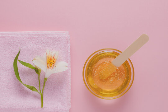 Liquid yellow sugar paste, wooden spatula, pink towel and flower on a pink background. Removing unwanted hair. Sugaring.Depilation. Epilation. Beauty.