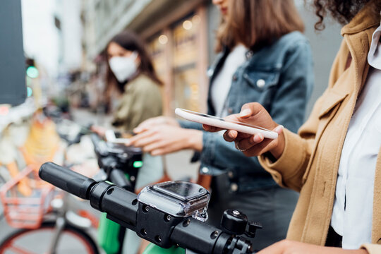 Woman unlocking bicycle through smart phone with friends standing in background