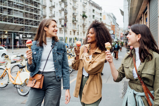 Smiling friends having ice cream while walking at city street - Powered by Adobe