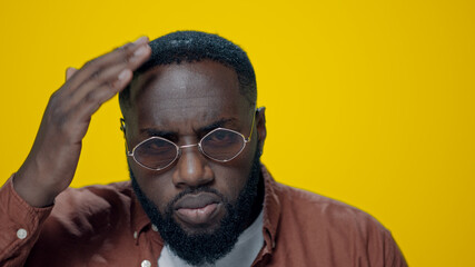 Portrait of serious african american man checking beard on yellow background. 