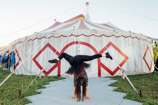 Female acrobat stretching legs while doing handstand on footpath