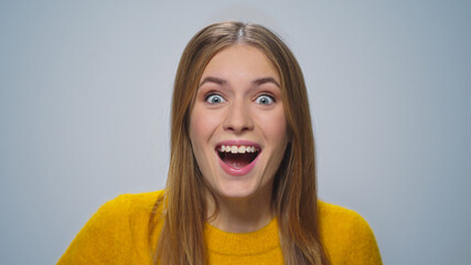 Portrait of happy attractive woman showing yes gesture on grey background.