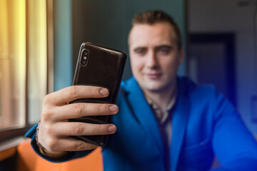Close-up, businessman guy holds a black smartphone or mobile phone in his hand and takes a selfie or talks on a video link in a cafe