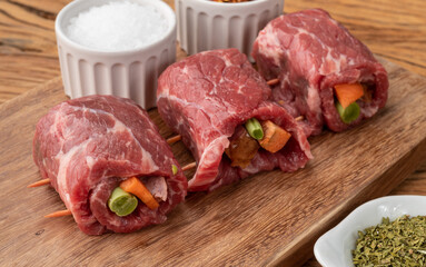 Rolled beef or roulade, vegetable and bacon stuffed meat over wooden table with seasonings