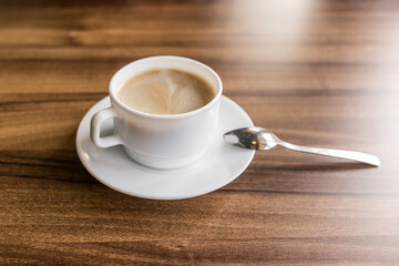 A cup of hot coffee on a saucer with a spoon stands on a wooden background of a table in a cafe