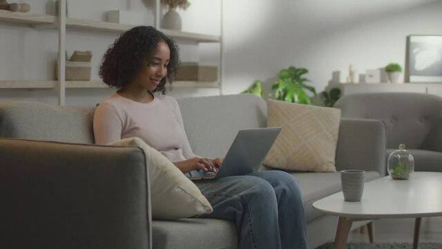 Young african american lady typing on laptop computer,chatting with friends or working remotely at home, free space