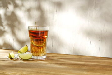 Glass of frozen tea drink on wooden table with bright white wall background. Natural sunlight and shadows.