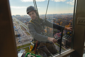 Man in a black helmet is hanging on a rope outside the window and washing the windows