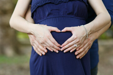 Future parents holding hand with heart shape on the prenancy woman belly with isolated blur garden background