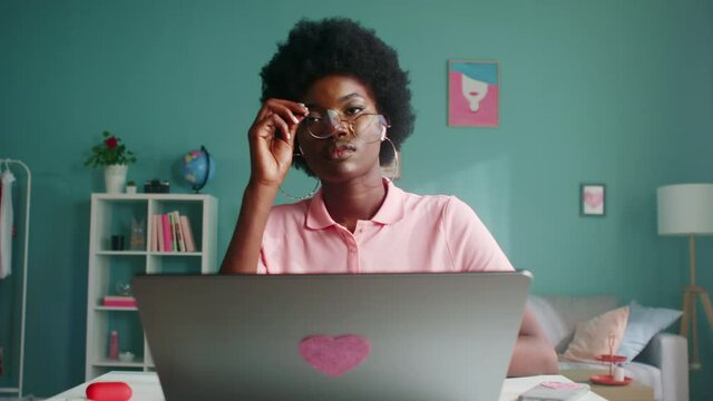 Young Afro-American woman, student, freelancer, is sitting at desk and working on laptop, searching information in the Internet, getting ready to new project, Foreground, Slow motion.
