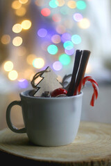 Mug filled with candy cane, cinnamon sticks and various Christmas decorations. Colorful bokeh lights in the background. Selective focus.
