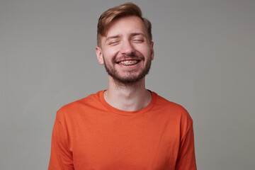 Studio portrait of young bearded man, wears casually posing over gray studio background smiles...