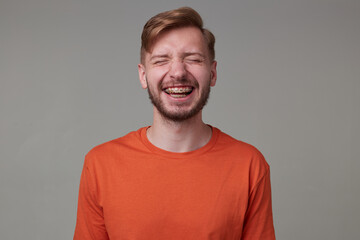 Studio portrait of young bearded man, wears casually posing over gray studio background smiles broadly and showing his teeth to the world. isolated.