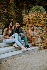 Young couple sitting on outdoor stairs on a autumn day and using mobile phone