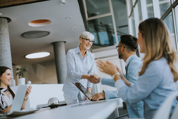 Mature business woman handshaking with young colleague on a meeting in office