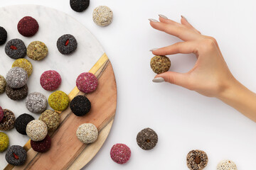 Colorful vegan candies energy balls on plate with womans hand isolated on white 