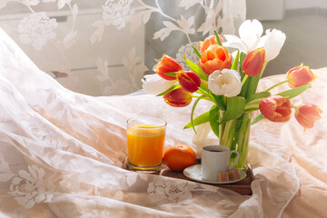 breakfast in bed with fruits, juice, coffee and flowers tulips on a tray. Romantic breakfast in bed