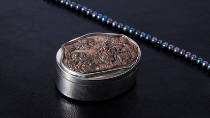 Old silver carved jewelry box on a black leather background. Retro composition.