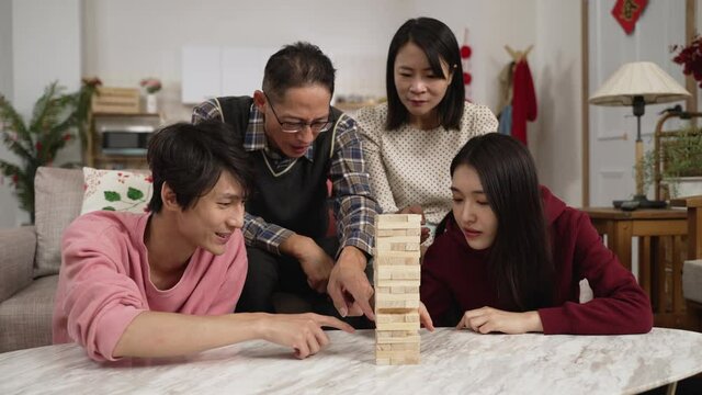 mother hitting father's hand to stop him and his son from affecting the player with finger pointing. daughter successfully removing and stacking the toy block