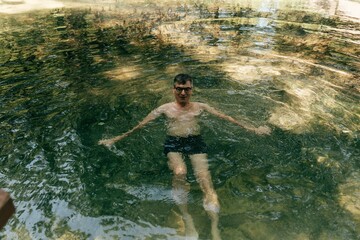 a man with glasses bathes in an icy transparent pond in summer