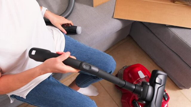 A housewife assembles a new vacuum cleaner. a woman is sitting on the couch and next to her is a box with a new vacuum cleaner. A woman in a white T-shirt and jeans. High quality 4k footage